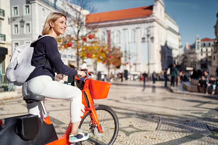 Woman enjoying a sunny day on a bike in Lisbon's historic streets, highlighting the vibrant charm of a private tour experience.