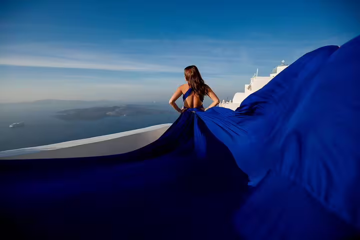 Woman in flowing blue dress overlooking Santorini's stunning caldera during private photography experience.