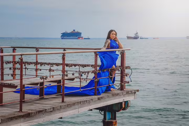 Woman in a flowing blue dress poses on a seaside pier with ships in the background in Ayia Napa.
