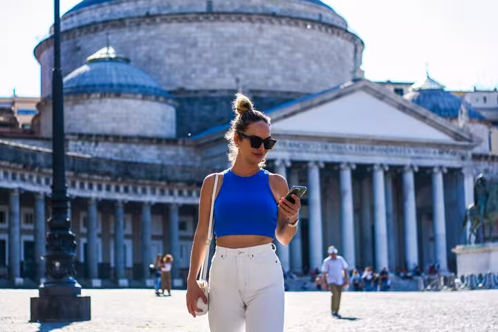 Woman in blue top and white pants walking in front of Basilica in Naples during a private photo shoot.