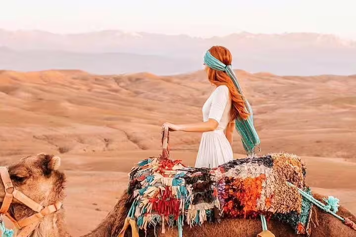 Woman on camel in Agafay Desert near Marrakech, scenic sunset camel ride tour with Atlas Mountains backdrop
