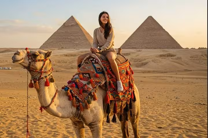 Woman on camel ride at sunset with Giza Pyramids on half-day tour in Cairo, including lunch and photo stops