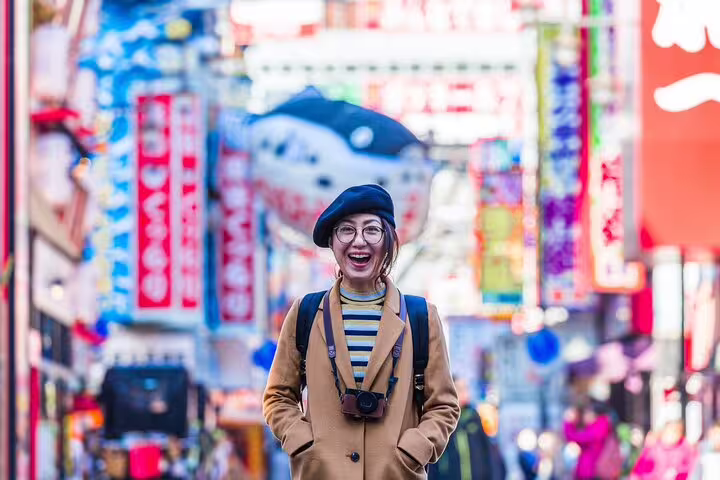 Smiling woman with camera explores vibrant streets of Osaka on private photoshoot tour.