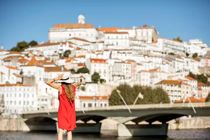 Woman in red dress and sunhat admiring Coimbra's historic cityscape during a private religious day trip from Lisbon.
