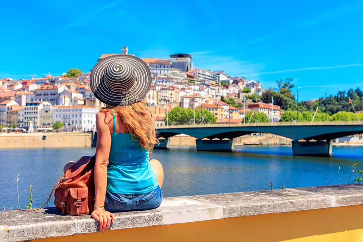 Woman in hat enjoying the scenic view of Coimbra's riverside on a sunny day during a private Lisbon day trip tour.