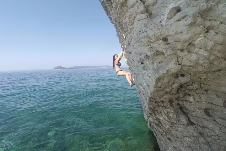 Woman deep water solo climbing a seaside cliff near Split, Croatia above clear Adriatic water
