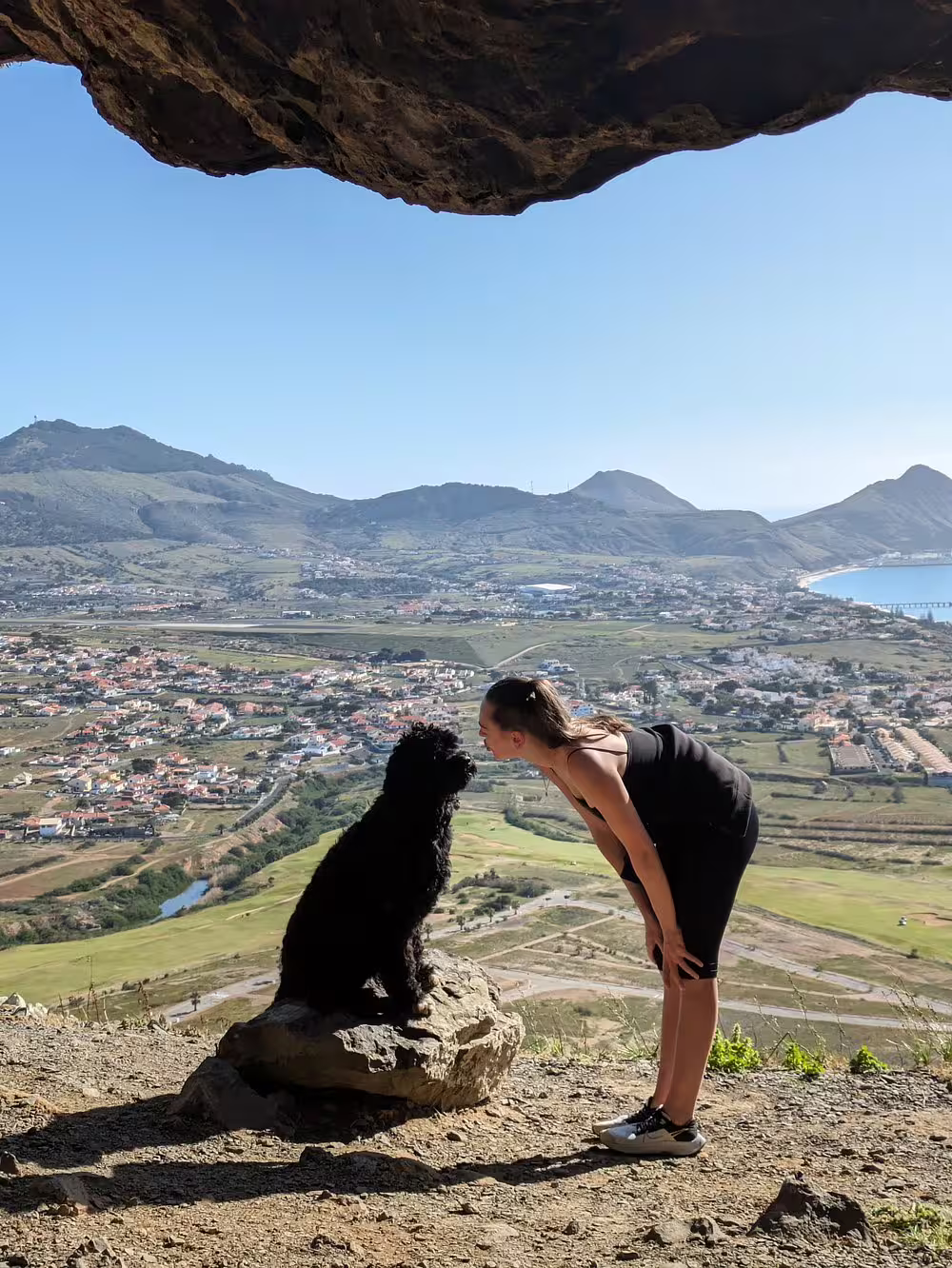 Woman and dog enjoy panoramic mountain views from a cave on the Ana Ferreira Caves & Peaks Trek in Porto Santo.