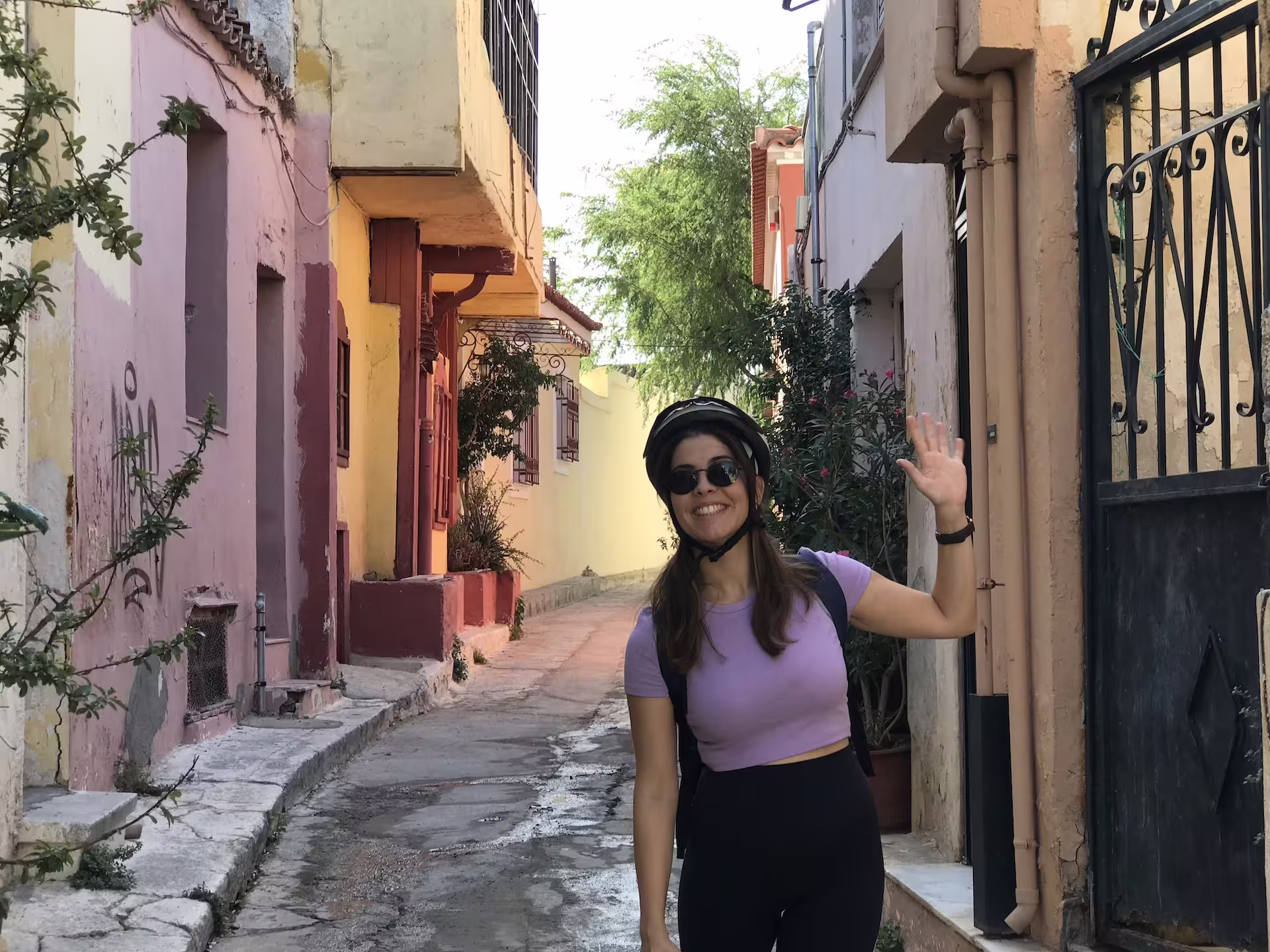 Woman waving in a charming, colorful alley in Athens, enjoying an e-bike tour experience.