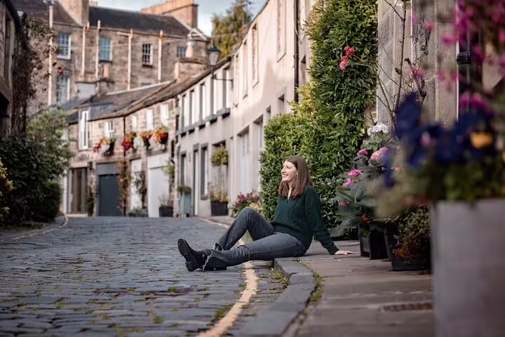 Woman sitting on a charming cobblestone street in Edinburgh with colorful flowers and historic architecture.
