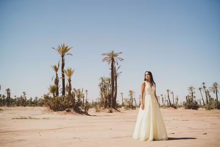 Woman in an elegant dress posing in Marrakesh desert landscape with palm trees, perfect for vacation photography.