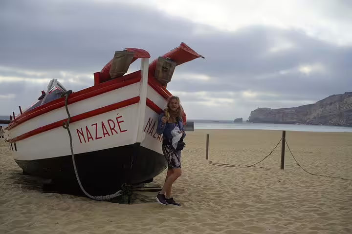 Woman standing by a traditional fishing boat on Nazaré beach, perfect stop on a full-day private tour from Lisbon to Óbidos and Fátima.