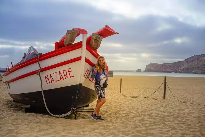 Woman standing by traditional fishing boat on Nazaré beach, highlighting picturesque Portuguese coastal tour destinations.