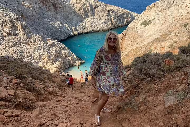 Woman in floral dress hiking down to the turquoise waters of Seitan Limania beach surrounded by cliffs.