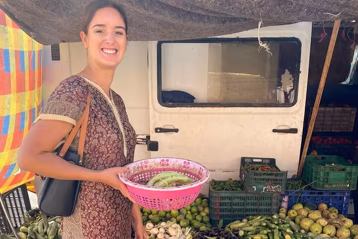 Smiling woman holding a basket of fresh vegetables at a local market during a cooking class tour.
