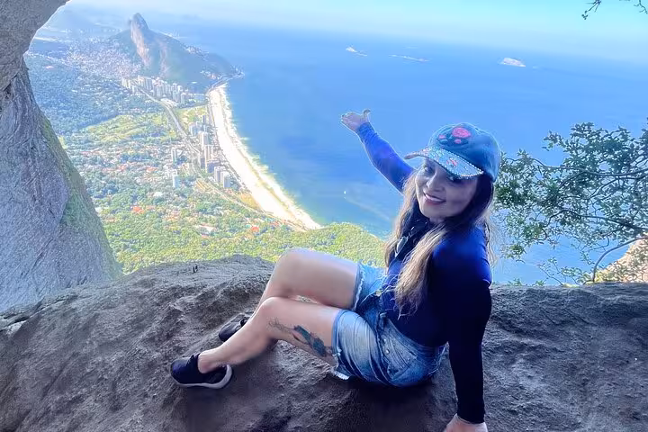 Smiling woman enjoys panoramic ocean and city views from Garganta do Céu during Pedra da Gávea hike.