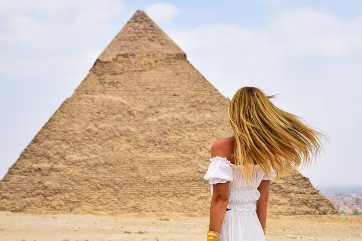 Woman with flowing hair faces the Pyramid of Giza during Sharm to Cairo by plane tour, pyramids and GEM day trip