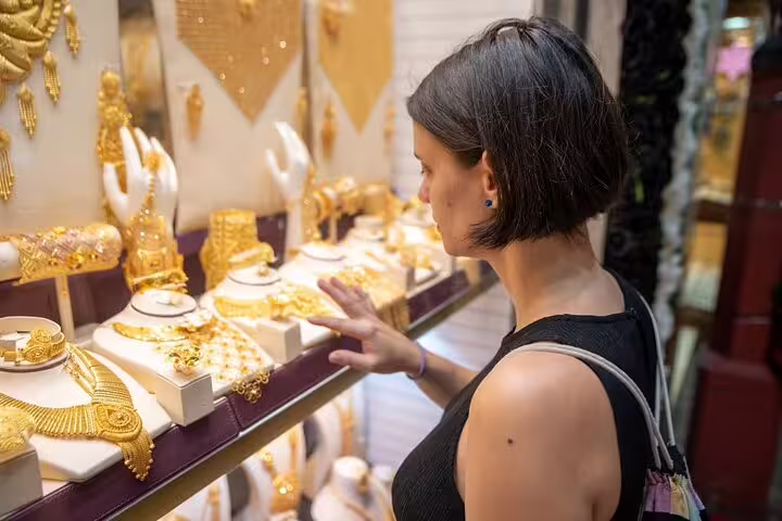 Woman admiring ornate gold necklaces in Dubai Gold Souk window on guided walking tour with local snacks and market visits