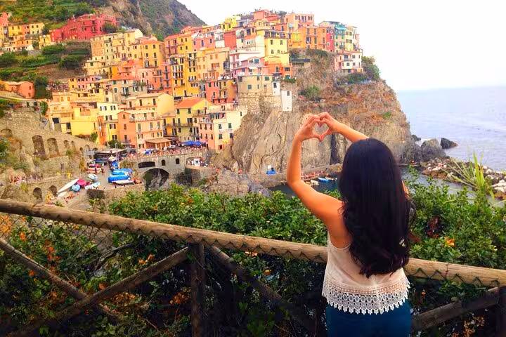 Back view of a woman forming a heart shape with hands overlooking the vibrant village of Cinque Terre.