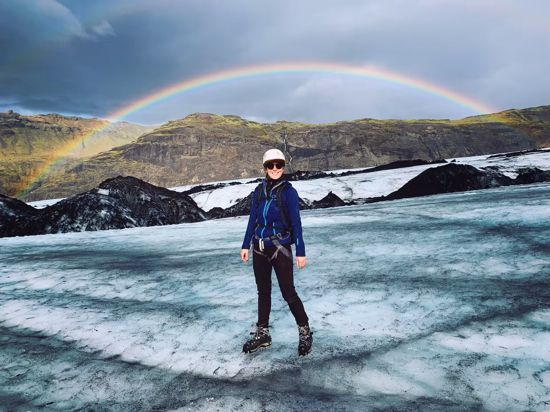 Woman exploring Icelandic glacier under a vibrant rainbow during women-only Ring Road adventure tour.