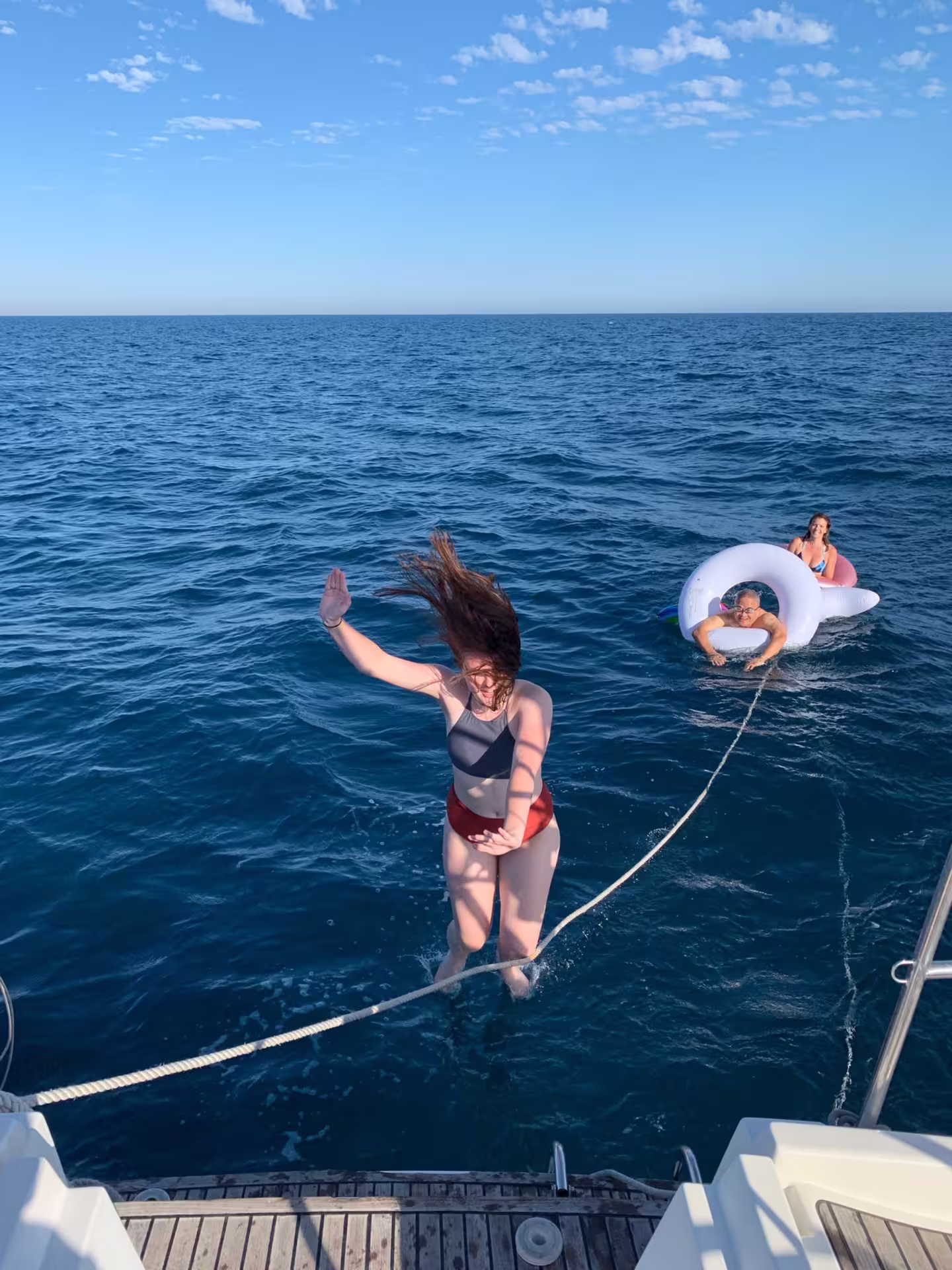 Woman enjoying a sunny day on a sailboat in Barcelona, jumping into the sea, highlighting a fun-filled private sailing experience.