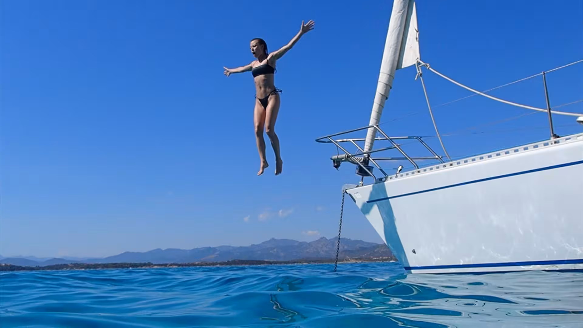 Woman joyfully jumping from yacht into crystal-clear sea on San Teodoro sailing adventure.