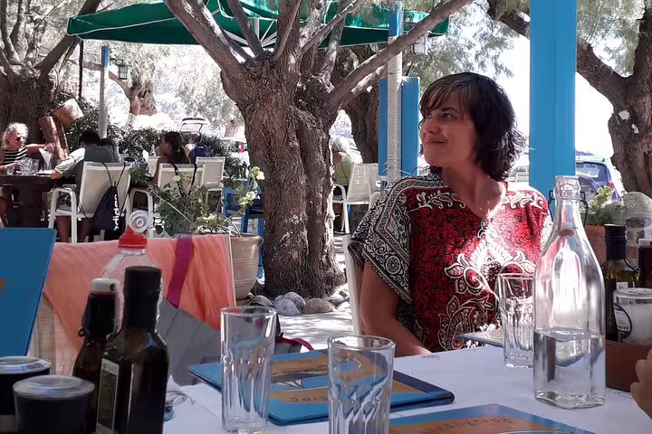 A woman enjoys a sunny lunch at a charming outdoor cafe on the South Coast of Crete during a private tour from Chania.