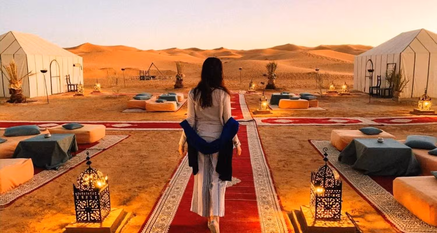Woman walking through a lantern-lit desert camp in Merzouga during a Marrakech 3-day safari tour.