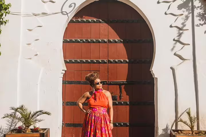 Woman in vibrant attire posing confidently by a large traditional Moroccan door in Marrakesh, Egypt.