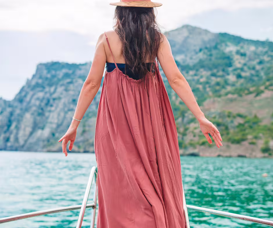 Woman in flowing dress enjoys breathtaking ocean and mountain views from a boat on the Teide y Delfines adventure.