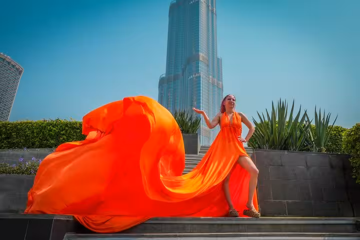 Elegant woman in an orange flying dress poses near Burj Khalifa, ideal for Instagram videography in Dubai.