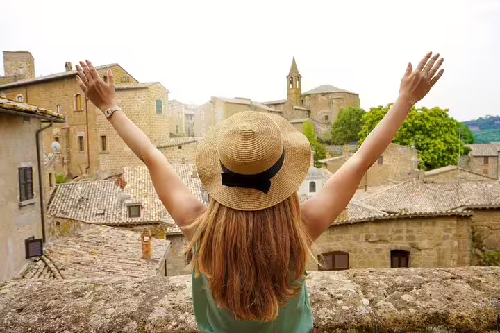 Woman in straw hat joyfully overlooking Orvieto's historic skyline on a private full-day tour from Rome with lunch included.