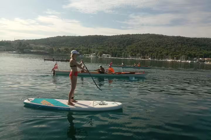 Woman paddling on a stand up paddleboard in Split bay, calm Adriatic water with boats and green hills