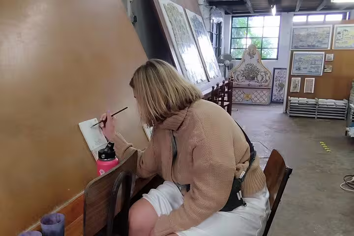 Woman painting tiles in a cozy studio during a private workshop on a Sesimbra tour with wine tasting experience.