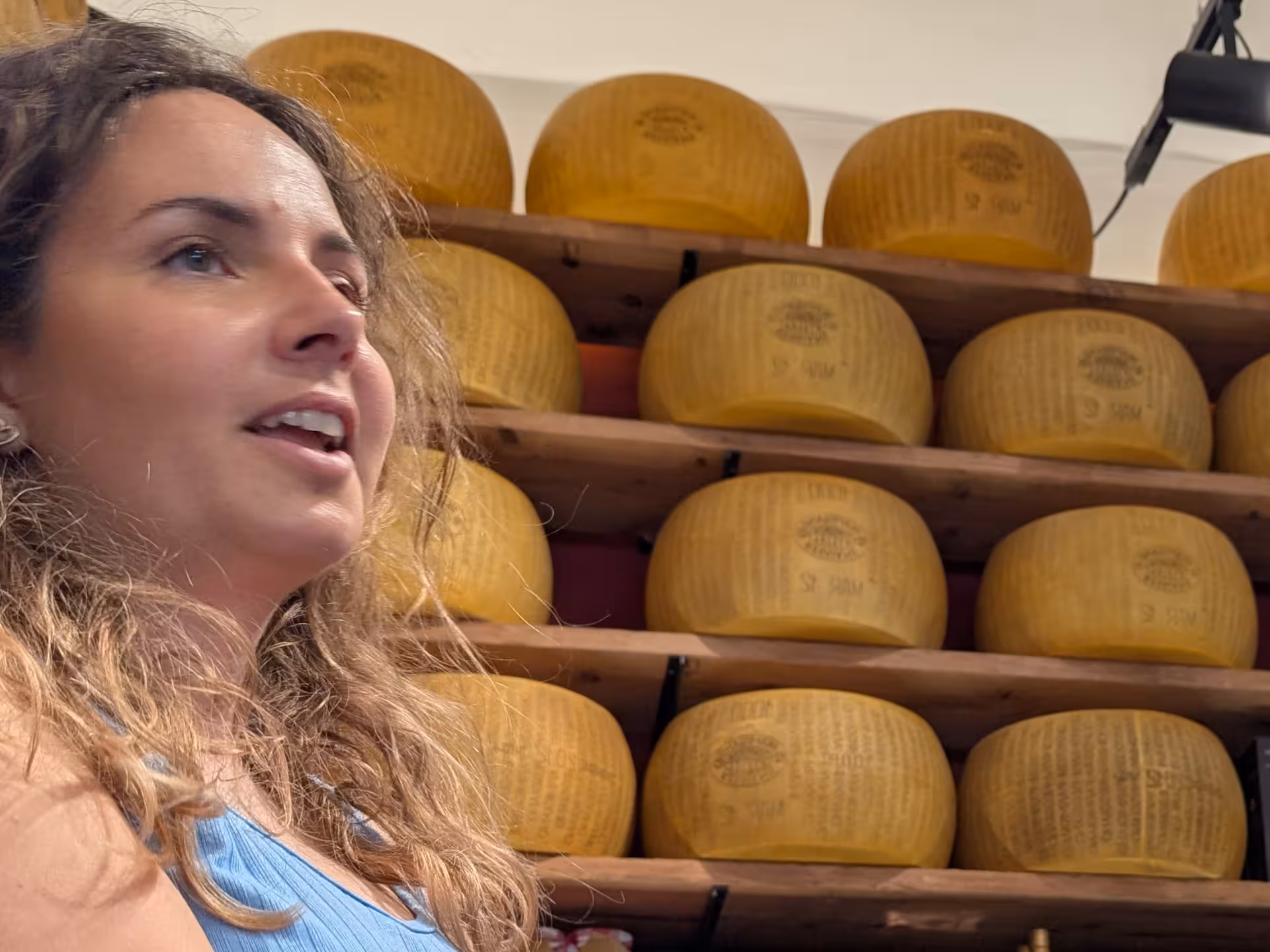 Woman in Parma shop with shelves of Parmigiano Reggiano wheels, highlighting wine tasting and local delicacies.