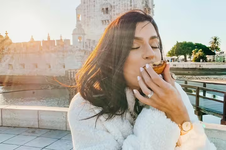 Woman enjoying a pastel de nata near the iconic Belém Tower during a bright afternoon in Lisbon.
