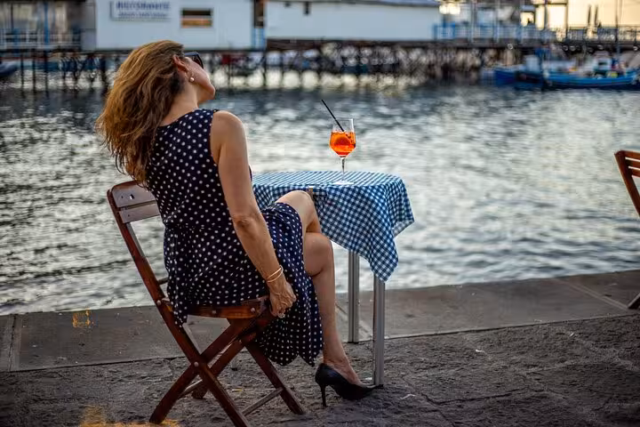 Woman in polka dot dress enjoying a seaside drink at sunset in Sorrento on the Amalfi Coast.