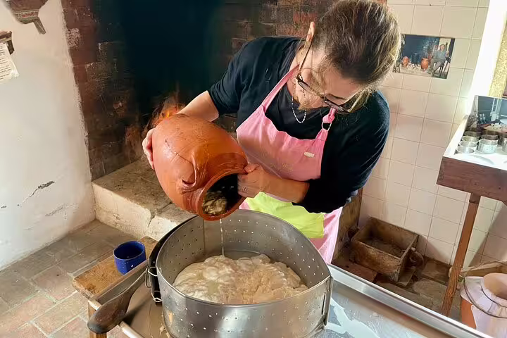Woman in pink apron pouring liquid into cheese mold during hands-on Azeitão cheese workshop, part of a Sesimbra tour experience.