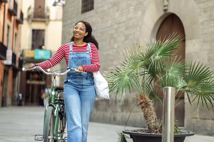 Woman enjoying a private bike tour in Barcelona, walking her bike through charming streets near historic architecture.