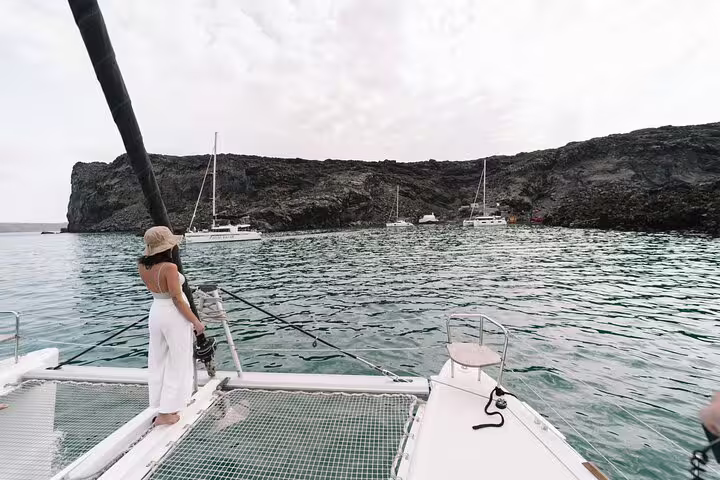 A woman stands on a catamaran in Santorini, admiring the serene waters and rugged cliffs on a private cruise.