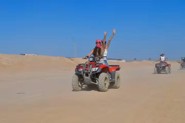 Woman riding quad bike across Sharm El Sheikh sand dunes on private VIP ATV safari, hands raised in fun