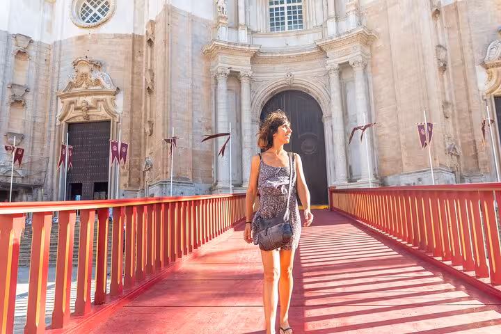 Woman walking on a red bridge in front of Cadiz Cathedral during a sunny private city tour.