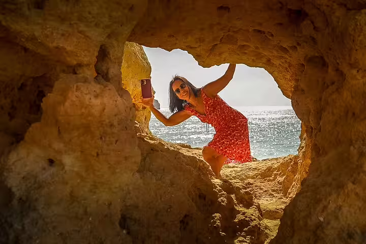 Woman in a red dress explores Algarve's coastal caves with ocean view, part of Seville to Lisbon scenic transfer tour.