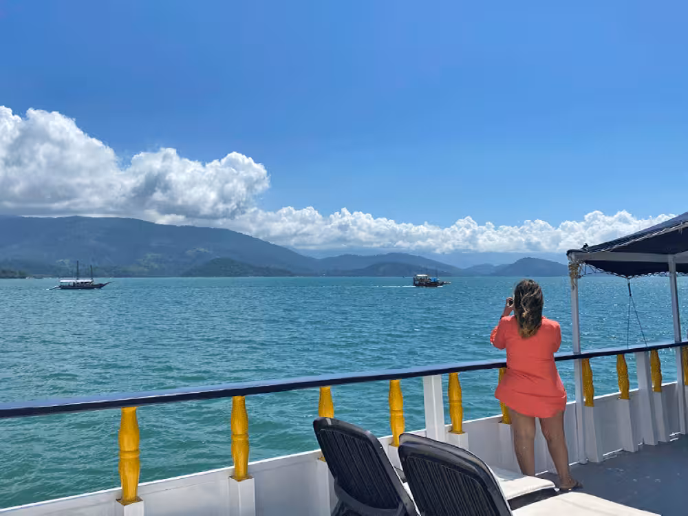 Woman in red dress enjoys scenic mountain views on a boat during a five-hour caipirinha cruise.