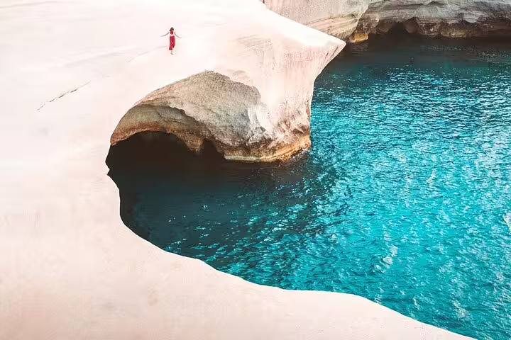 Woman in red dress exploring stunning white cliffs and turquoise waters on a private sunset motorboat tour in Milos.