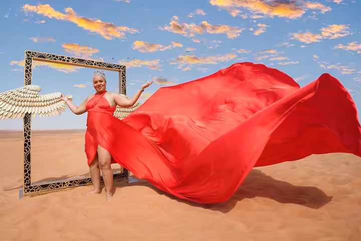Woman in a vibrant red dress with angelic wings poses in Dubai's desert, showcasing the flying dress tour's allure.