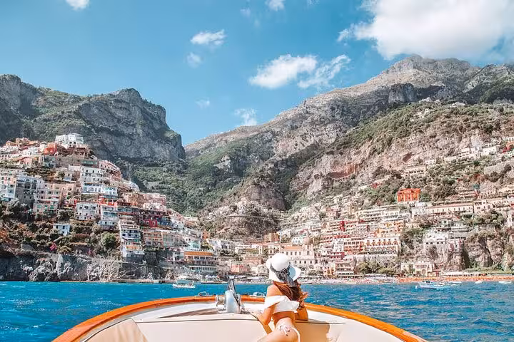Woman relaxing on a boat, enjoying breathtaking views of Positano's vibrant cliffs on the Amalfi Coast.