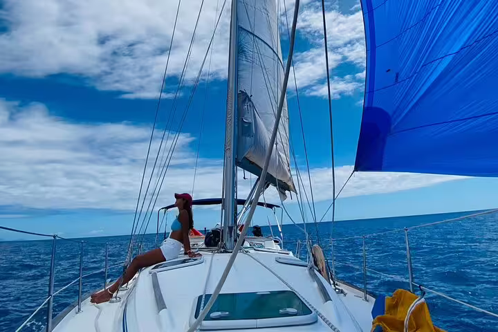 A woman relaxes on a yacht deck under clear skies during a private sailing cruise, showcasing Madeira's stunning seascape.