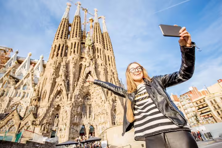 Woman taking a selfie in front of Sagrada Familia, enjoying a private food and drink tasting tour with skip-the-line access.