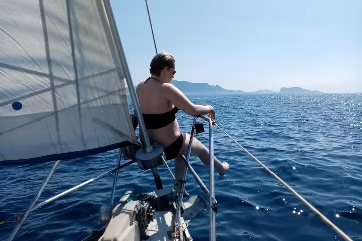 Woman sitting on sailboat bow near Marseille, enjoying windy Mediterranean sea and Calanques coastline views