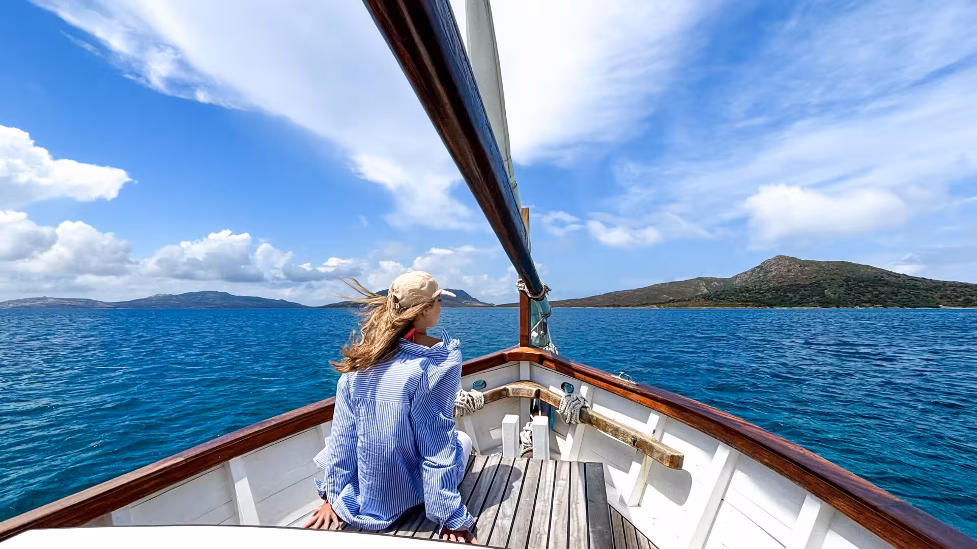 Woman relaxing on a sailboat enjoying stunning views of Asinara's turquoise waters and scenic coastline from Stintino.